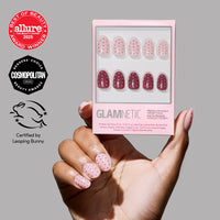A hand with pink nails and red polka dots holds a box of glamnetic Cute As Cherry Pie short oval press-on nails, showing red and pink polka dot designs. Allure, Cosmopolitan, and Leaping Bunny vegan cruelty-free logos are visible.
