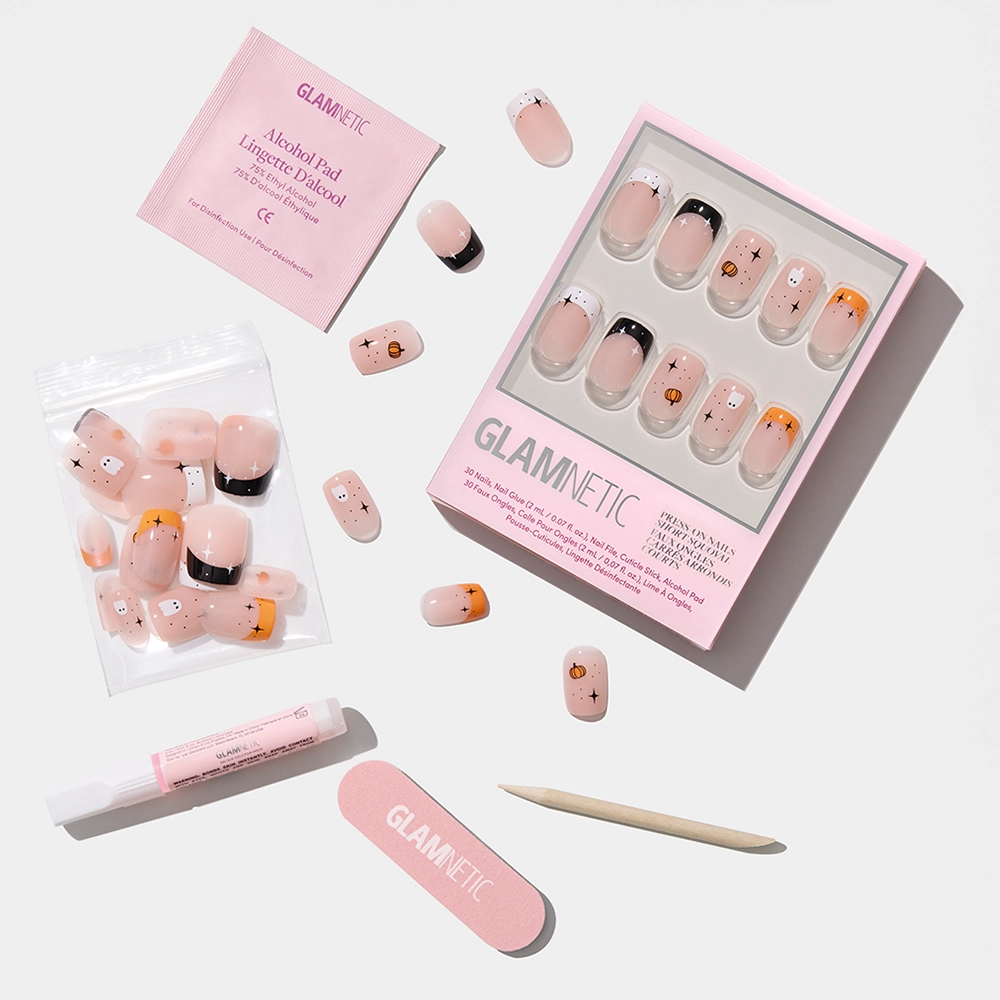 The glamnetic Tiny Pumpkin press-on nails set, featuring cute animal and ghost nail art, comes with an alcohol pad, nail glue, pink nail file, and wooden cuticle stick arranged neatly on a white surface. - Product image