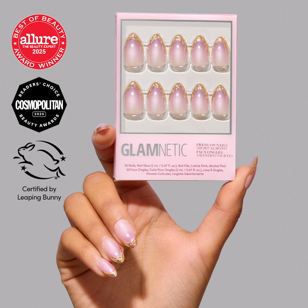 A hand holds a box of Glamnetic Tipped in Gold short almond press-on nails featuring a sheer pink base and gold French tips, accompanied by three beauty award seals. - Product image