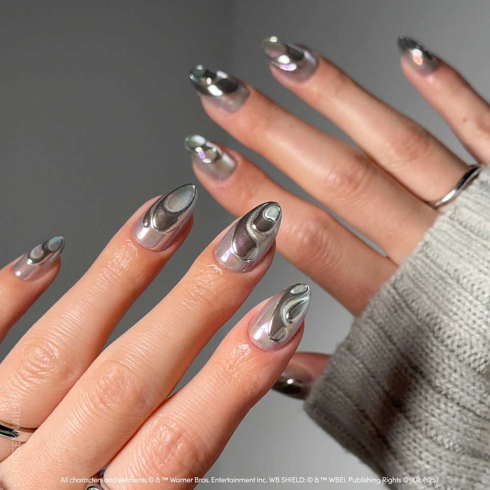 Close-up of hands with almond-shaped chrome nails in glamnetic’s Unicorn Blood, a shiny metallic silver with chrome swirls inspired by magical creatures. The person wears a gray knit sweater and a simple silver ring. - Product image
