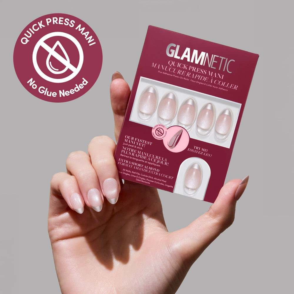 A hand with manicured nails holds a glamnetic Velvet Chrome Quick Press Mani box, displaying six pinkish nude stick-on nails. The box and a circular logo in the top left both state "No Glue Needed. - Product image