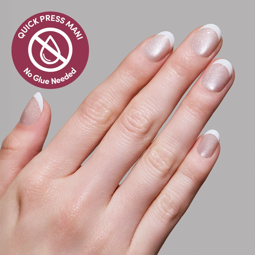 A hand with neatly manicured nails shows Velvet French press-ons by glamnetic: shimmery nude polish and white tips. A circular label reads Quick Press Mani, No Glue Needed, with a crossed-out droplet symbol. Background is light gray. - Product image