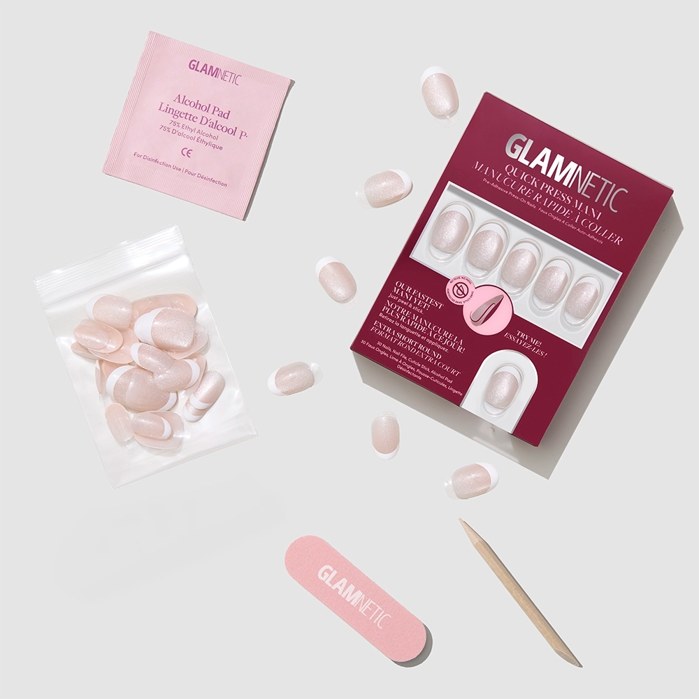A flat lay of glamnetic Velvet French press-on nails kit shows a maroon box with oval pink nails, nail file, cuticle stick, nail glue, alcohol pad, and extra nails in a clear bag on a light background. - Product image
