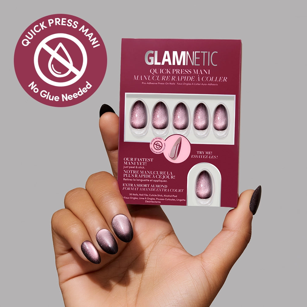 A hand with shimmery pink press-on nails holds a glamnetic Velveteen Trance Quick Press Mani nail set. A pink circular label reads QUICK PRESS MANI No Glue Needed, highlighting these easy-to-apply no-glue nails. The background is light gray. - Product image