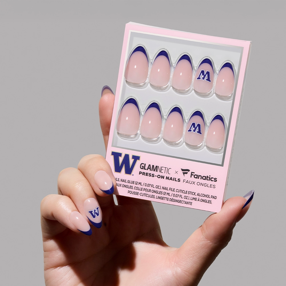 A hand holds the Washington Huskies Press-On Nail Set by glamnetic, featuring purple tips and W designs on some nails, against a neutral background. - Product image
