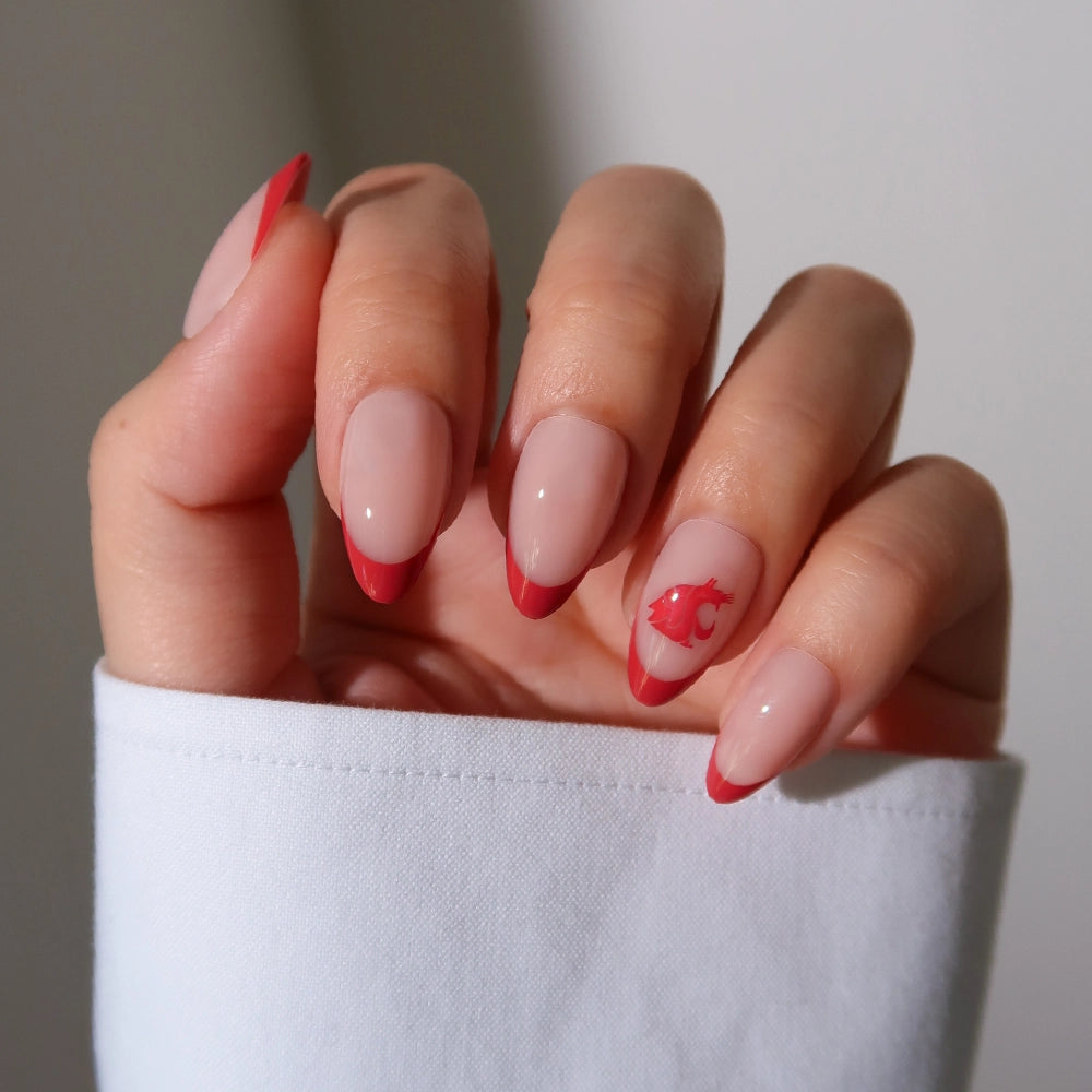 A hand displays the glamnetic Washington State Cougars Press-On Nail Set: almond-shaped nails with a nude base, red French tips, and a red fish accent on the ring finger. The person is wearing a white long-sleeve top. - Product image