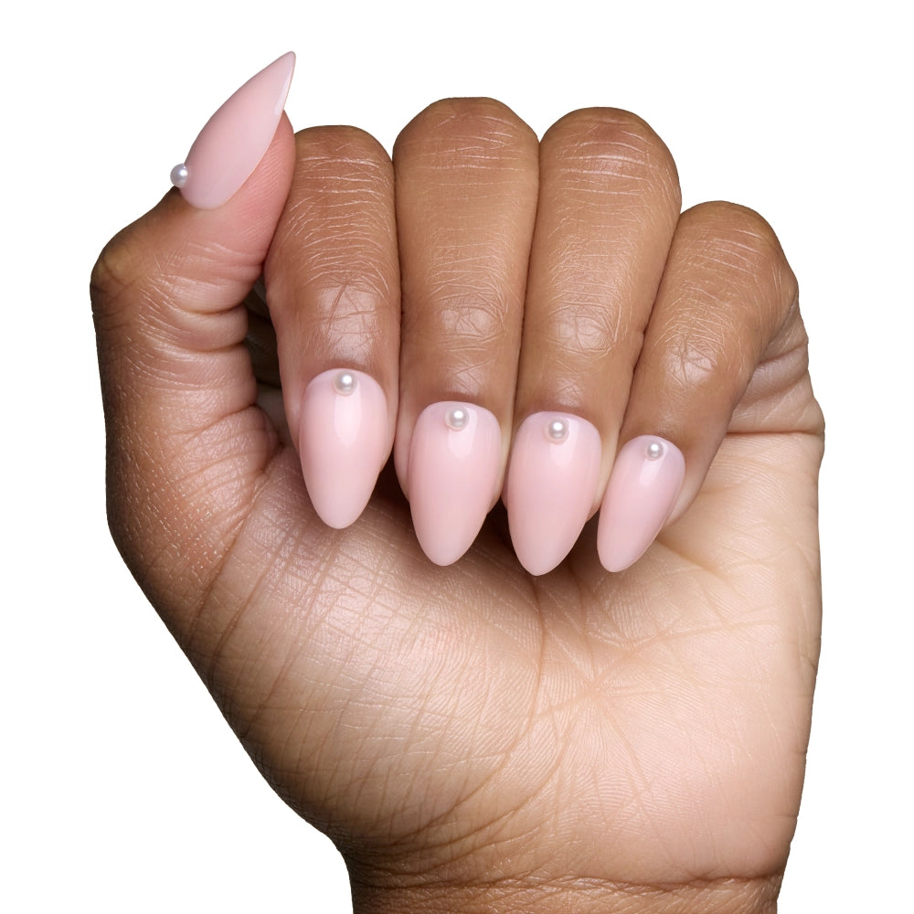 A hand with almond-shaped, pale pink nails from glamnetic’s Wifey set, each nail accented by a 3D pearl detail at the cuticle, is shown against a white background for a salon-quality look. - Product image