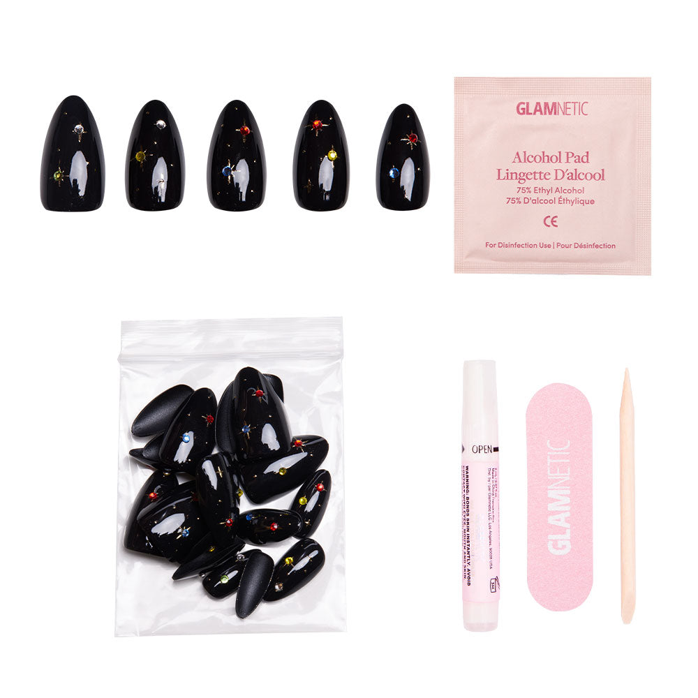 The glamnetic Winter Comet set includes black almond nails with celestial, colorful designs, nail glue, alcohol pad, pink file, cuticle stick, and extra nails—all in a clear bag on a white background. - Product image