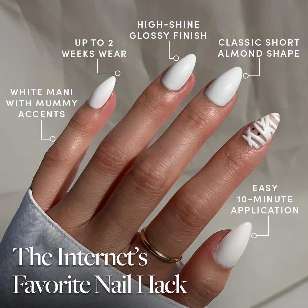 A hand displays glamnetic’s “Wrapped Up” press-on nails—short, almond-shaped, and glossy white—with one nail featuring a bold geometric mummy-inspired design. Text highlights their easy 10-minute application and long-lasting wear of up to 2 weeks. - Product image