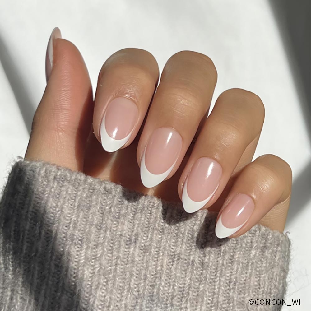 A hand with almond-shaped Ma Damn nails by glamnetic, showcasing a classic French manicure with a pale pink base and white tips, rests against a gray knitted sleeve. - Product image