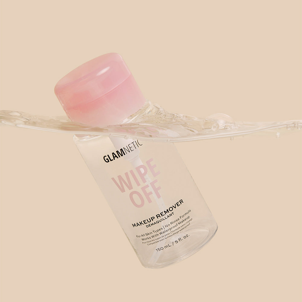 A clear bottle of glamnetic’s Wipe Off makeup remover with a pink cap is partly submerged in water, showing its strength as a skin cleanser and makeup remover—even for waterproof makeup—against a beige backdrop. - Product image