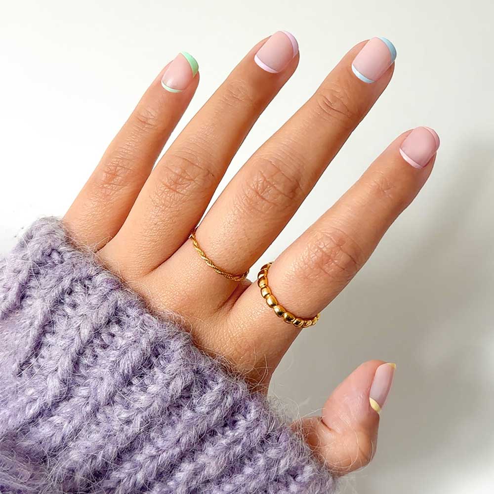 A hand with super short pastel French manicure nails, wearing two gold rings and a chunky light purple knit sweater, showcases glamnetics Tutti Frutti set against a white background. - Product image