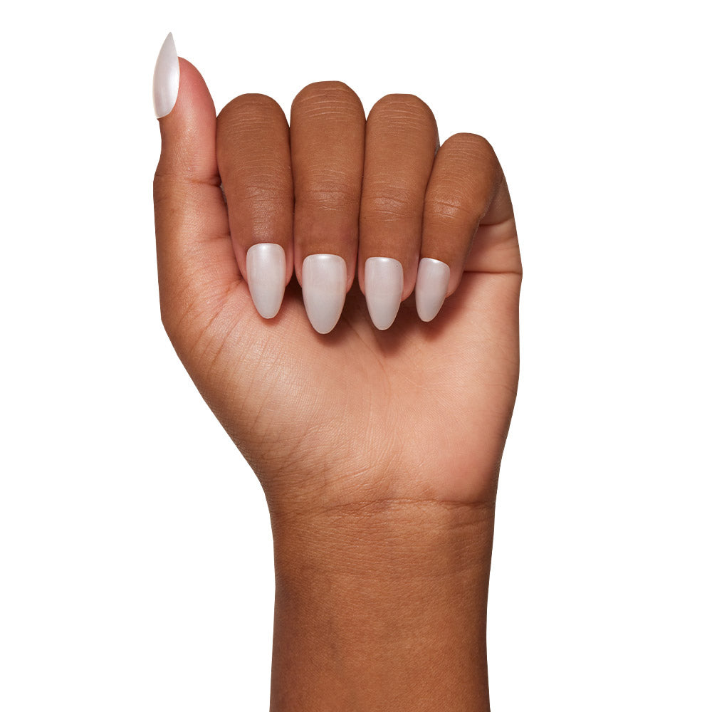 A medium brown hand with fingers curled inward showcases glamnetic’s Hailey Nail Set in a glossy pale pink Glazed Donut finish on long, almond-shaped nails against a white background. - Product image