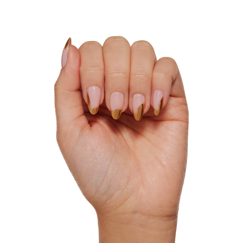 A hand showcases glamnetics Golden Touch nails: short almond shape in nude pink with abstract gold foil French tips, set against a white background. - Product image
