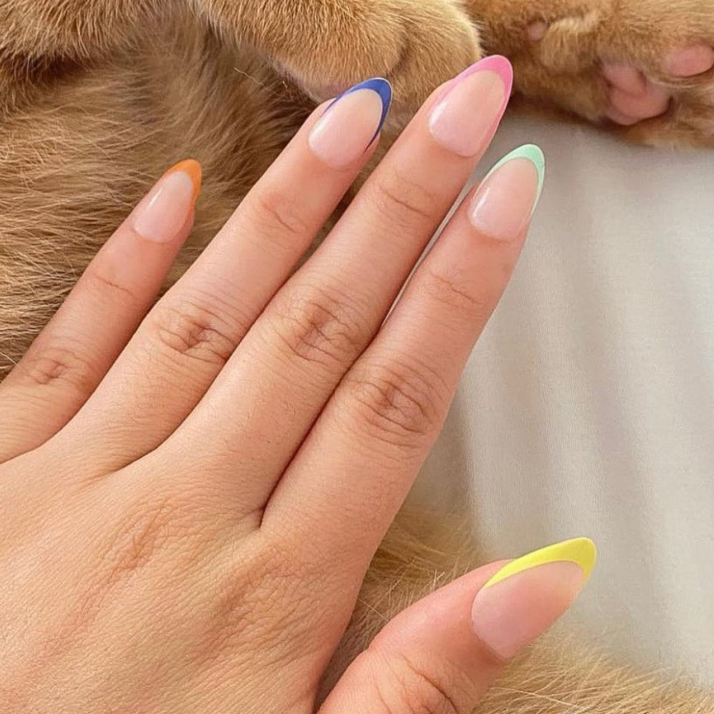 A hand with almond-shaped nails features a colorful French tip manicure using glamnetics Sprinkles. Each finger sports a different hue, and a cat’s fur can be seen in the background. - Product image