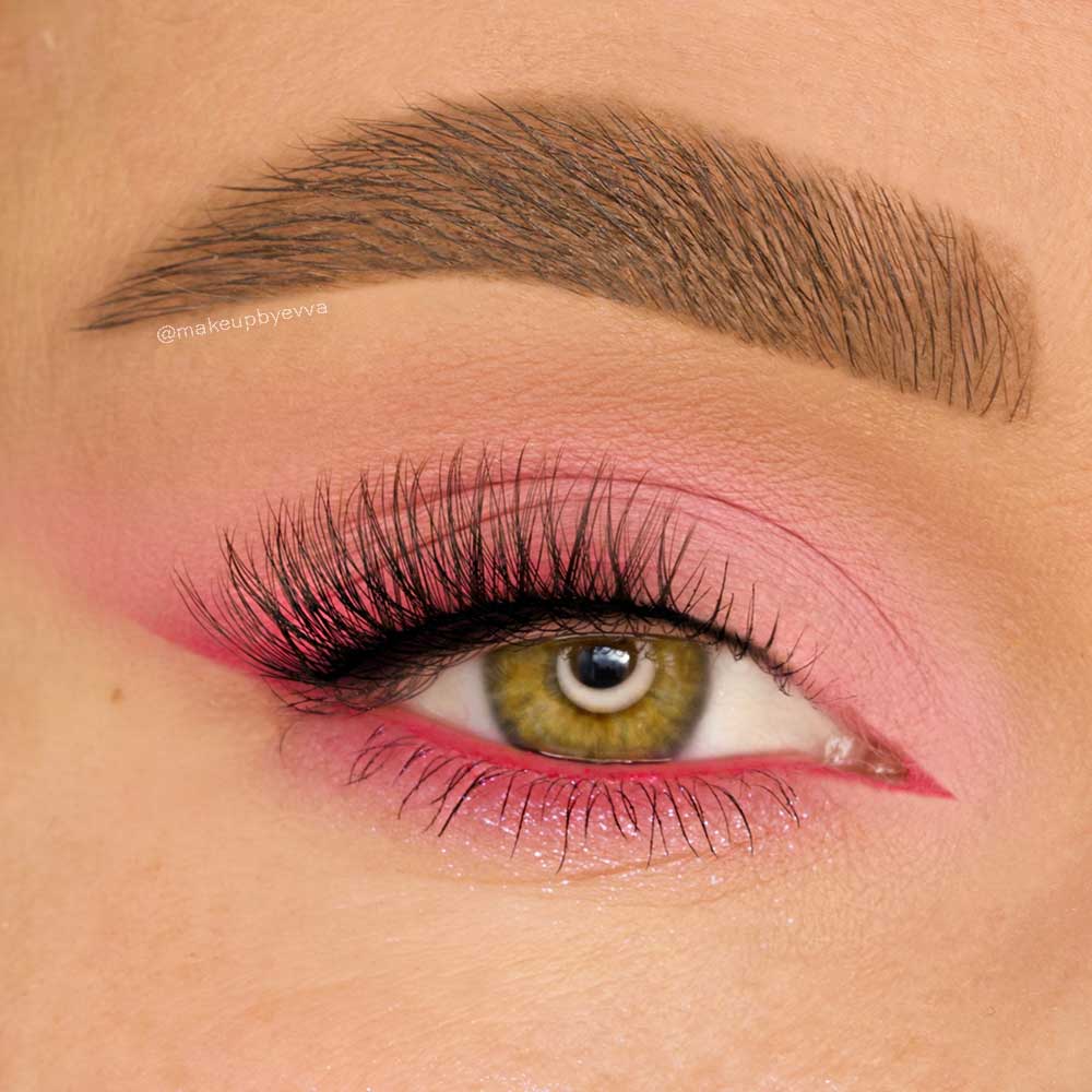 A close-up of a hazel eye with glamnetics Precious: bold pink eyeshadow, cat-eye winged liner, long voluminous lashes, and defined brows. Pink tones accentuate the eyelid and lower lash line for a striking effect. - Product image