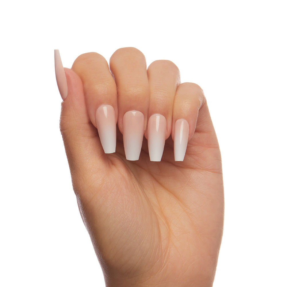 A hand showcases glamnetics Creme de Nude nails—long, coffin-shaped with a soft pink-to-white ombre and glossy finish—against a plain white background. - Product image