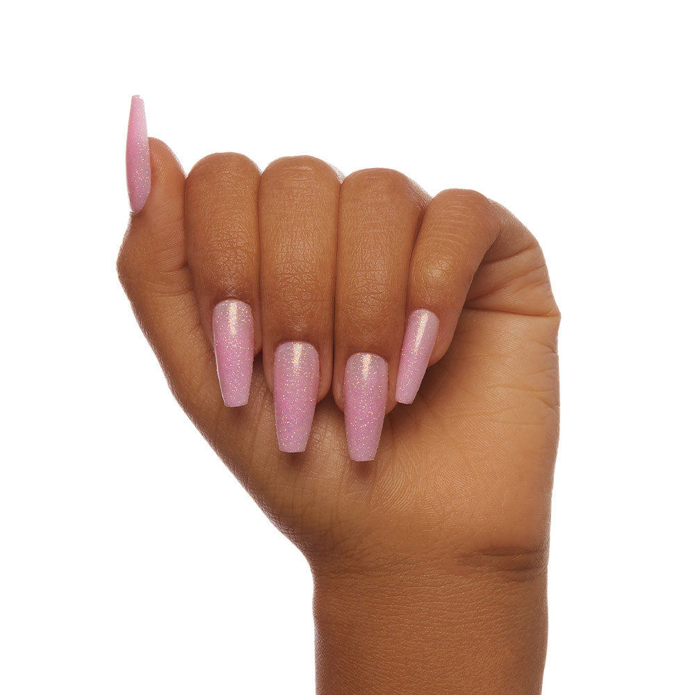 A hand with medium brown skin shows a fist, displaying glossy, shimmery light pink “Juicy” nails by glamnetic with early 2000s vibes on long, square tips, all set against a white background. - Product image