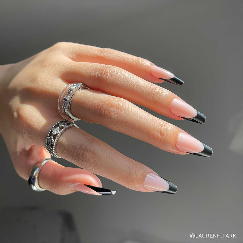 A hand showcases glamnetic’s Rogue nails—long, coffin-shaped with black French tips—accessorized by silver rings and set against a neutral background. - Product image