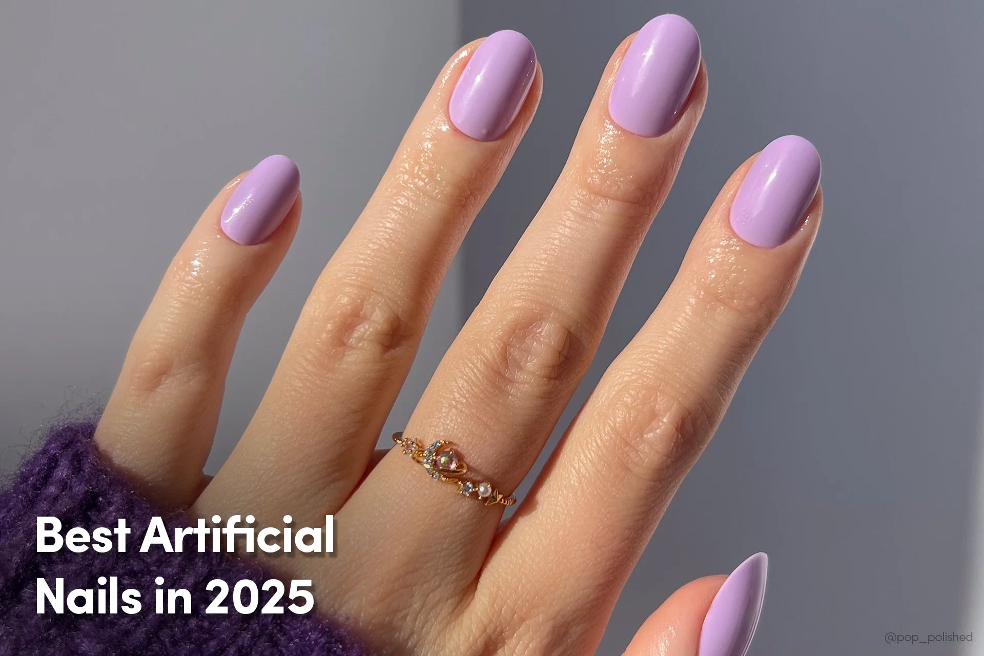 Hand with short, oval-shaped artificial nails painted in glossy lavender, wearing a gold gemstone ring, with the text “Best Artificial Nails in 2025”.