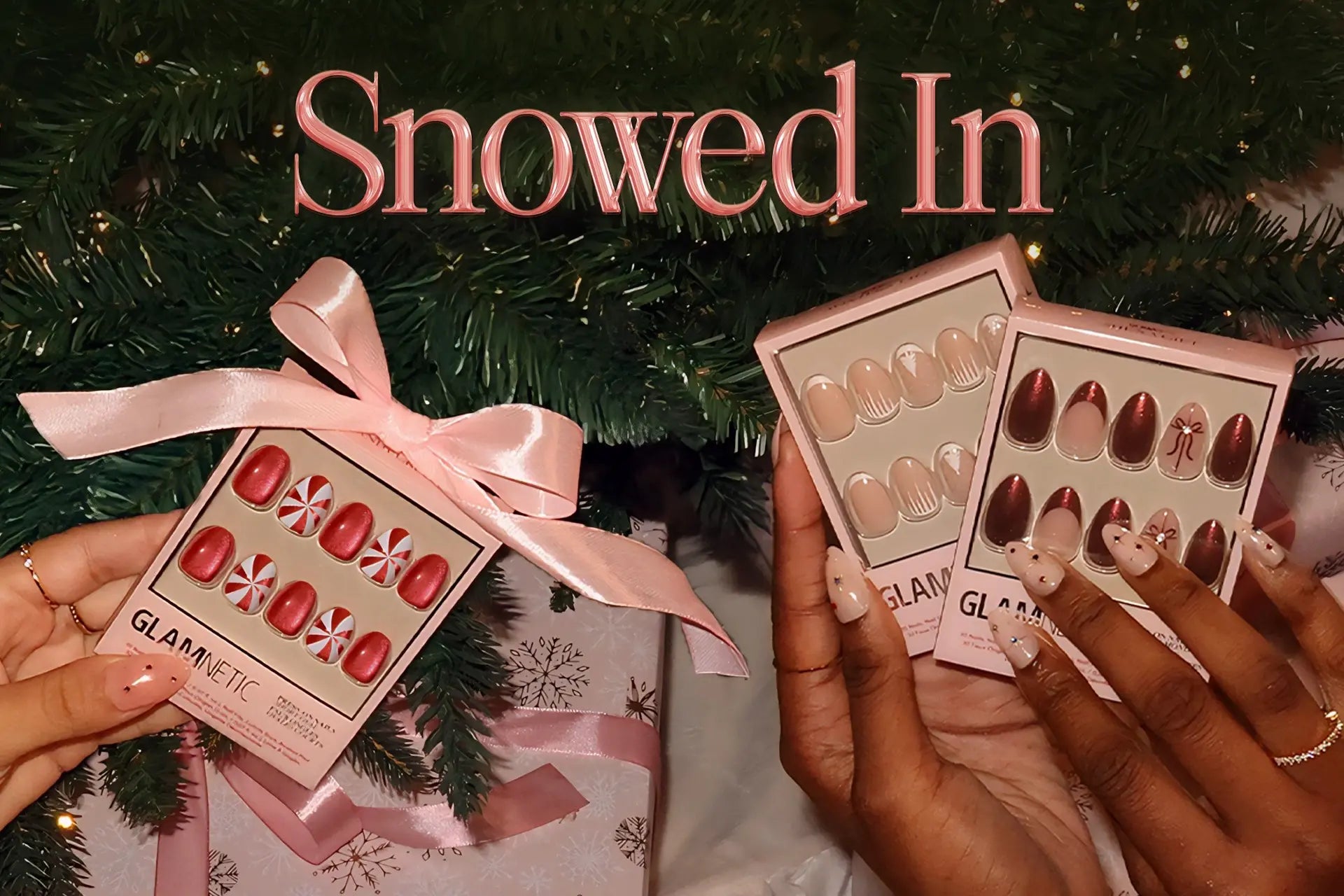 Hands holding Glamnetic holiday press-on nail sets in front of a Christmas tree with gifts, under the text ‘Snowed In.