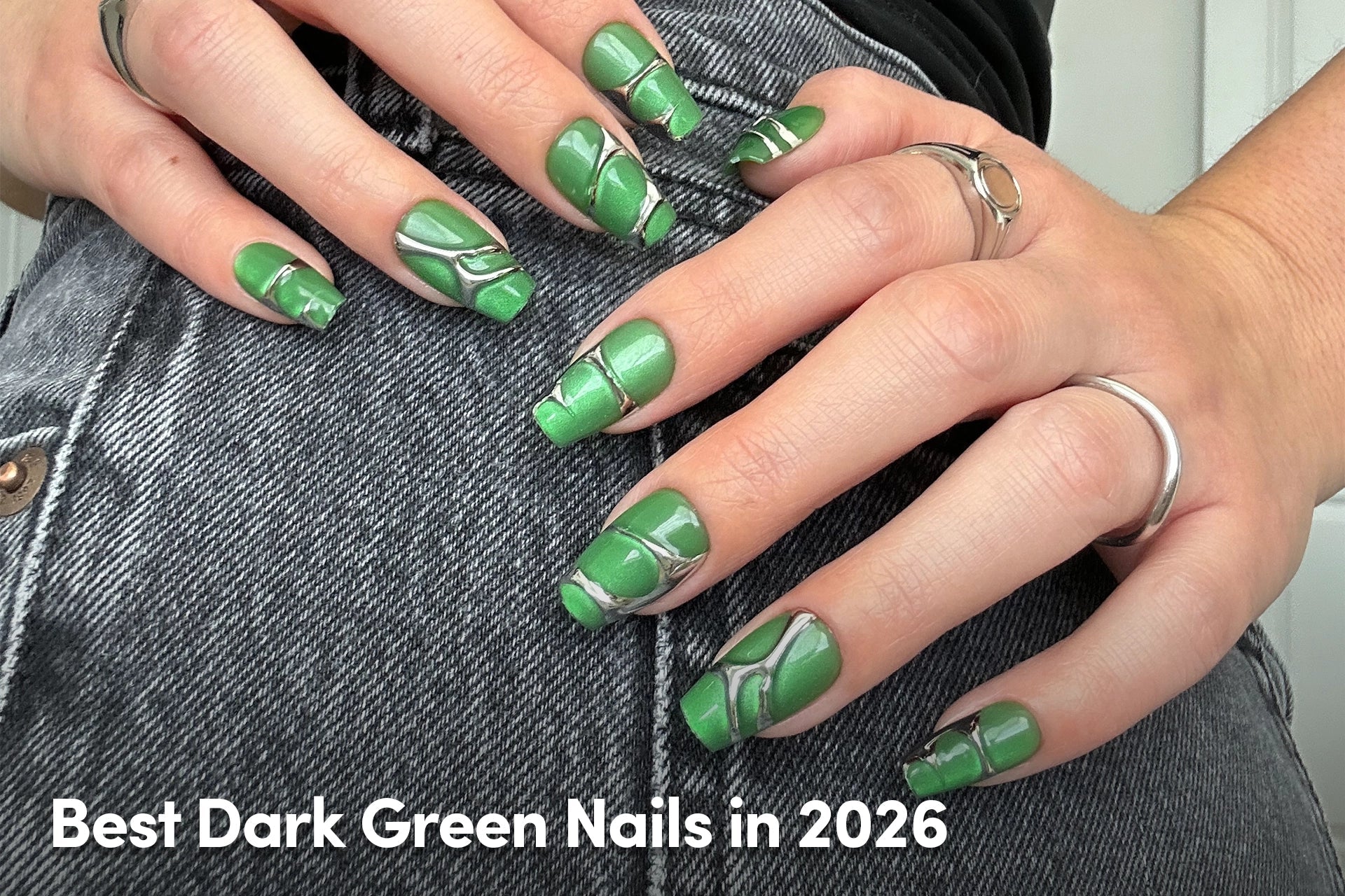 Close-up of hands with glossy dark green nails featuring abstract silver line designs.