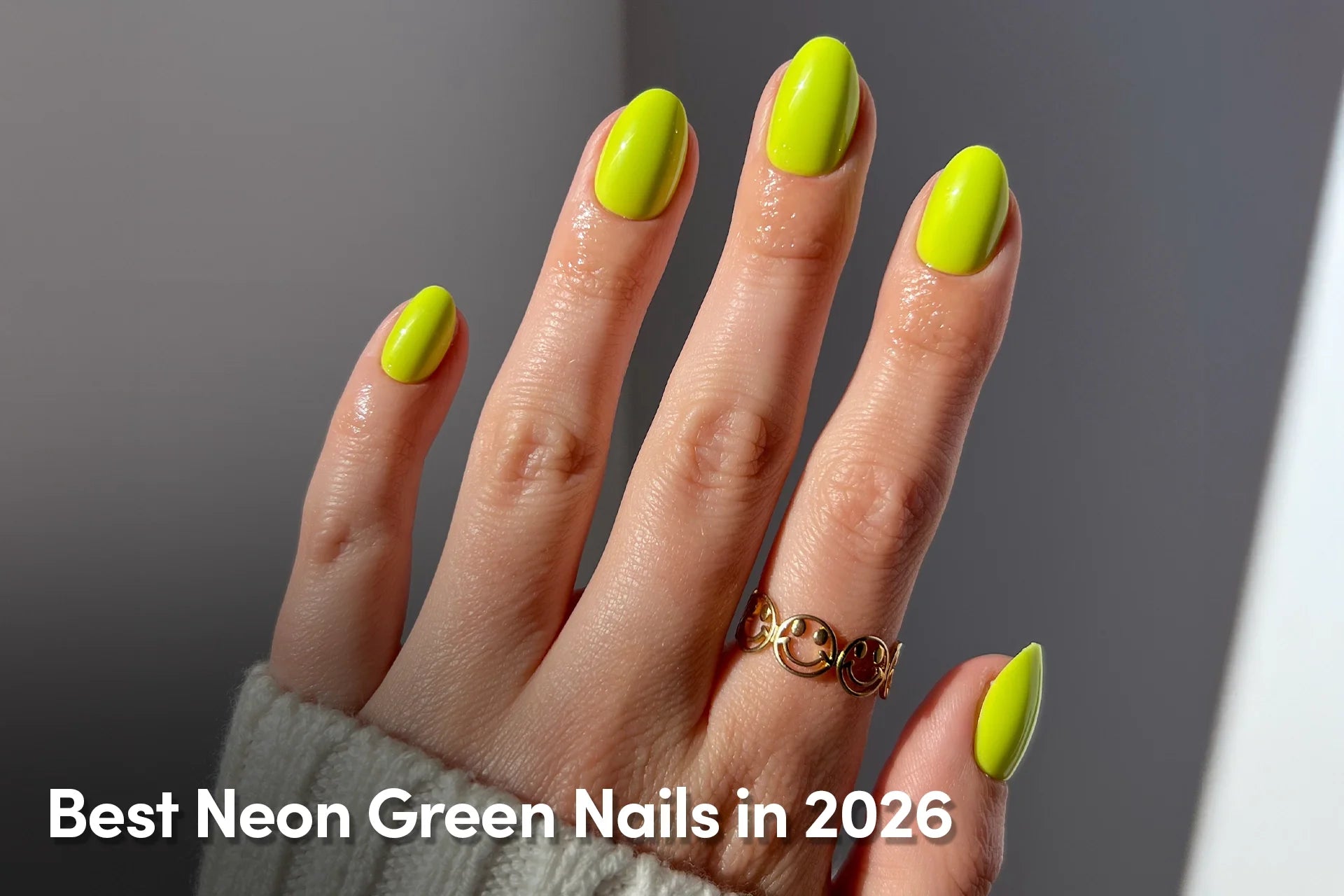 Hand with bright neon green oval-shaped nails and a gold smiley-face ring under natural light.