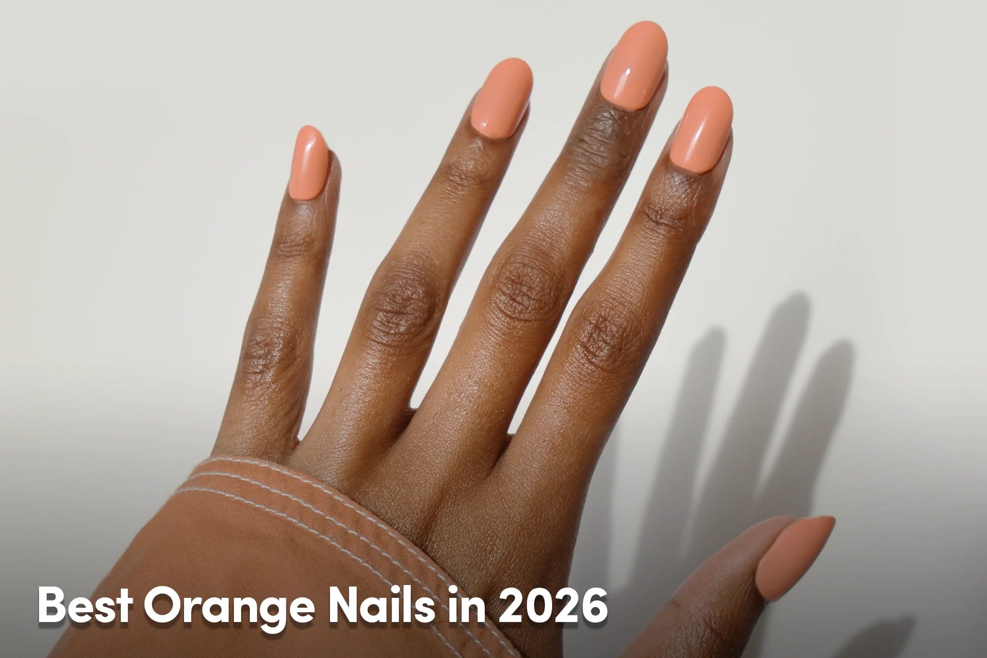 Hand with glossy orange almond-shaped nails against a neutral background.