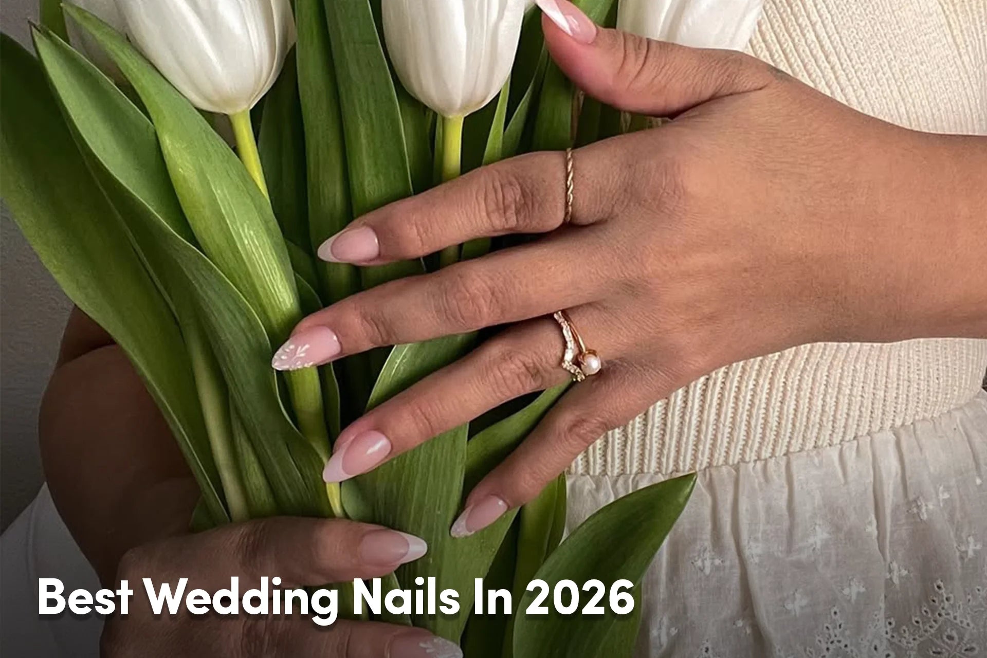 Hand with soft pink French tip nails holding white tulips.