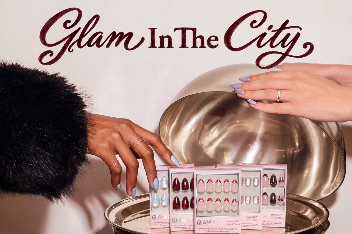 Glamnetic press-on nails displayed on a metallic tray with two hands, featuring soft pink, red, blue, and brown nail designs. Decorative “Glam In The City” text appears at the top.