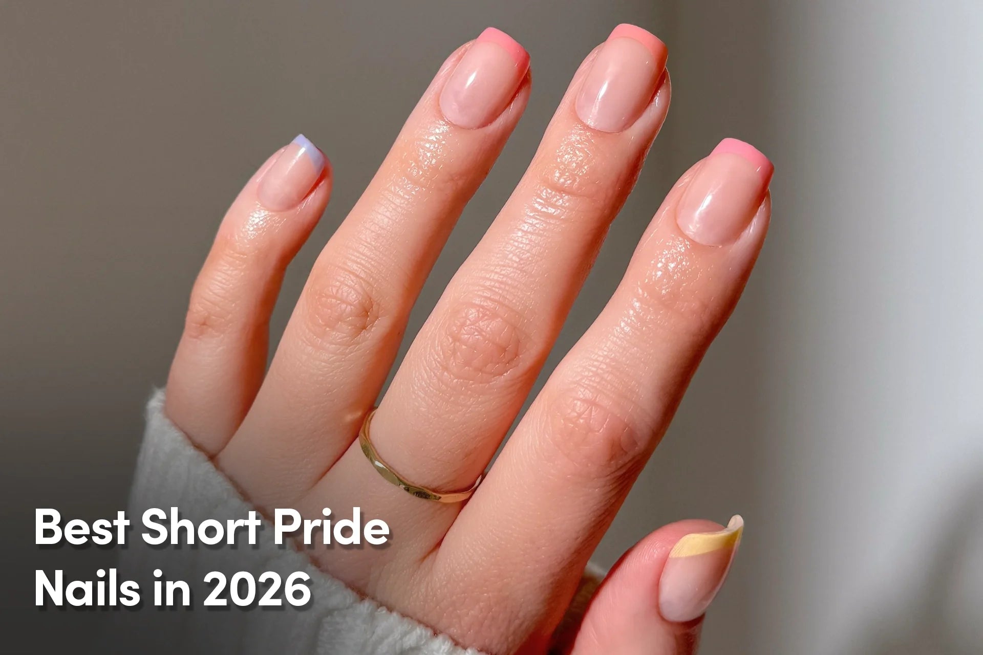 Short nude nails with pastel rainbow French tips on a hand.
