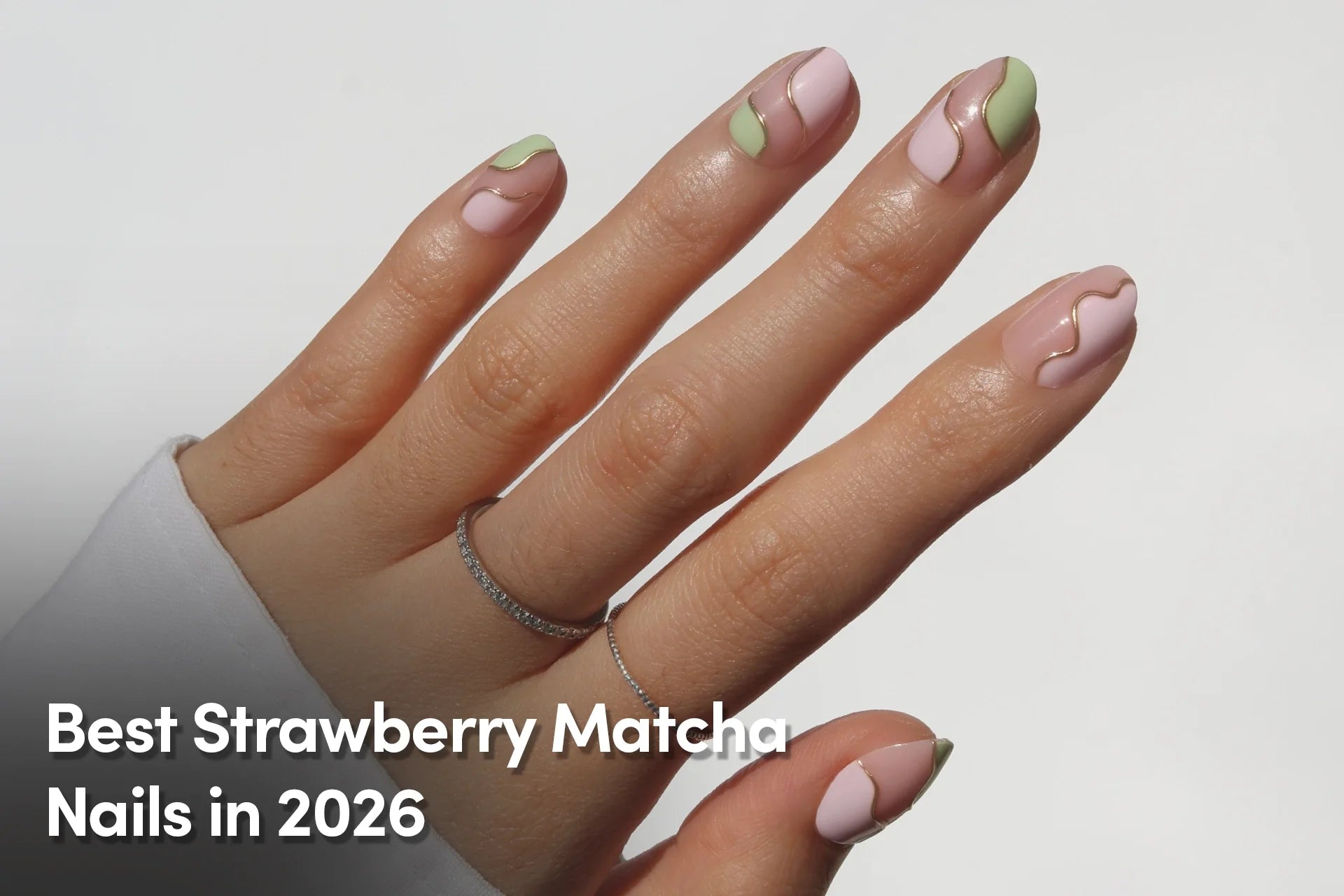 Hand with pastel pink and matcha green swirl nail art and gold accents.