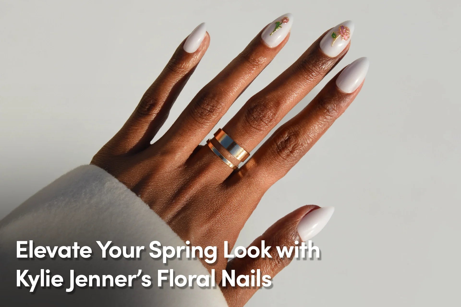Hand with glossy white almond-shaped nails featuring delicate floral nail art, promoting spring-inspired nail designs.