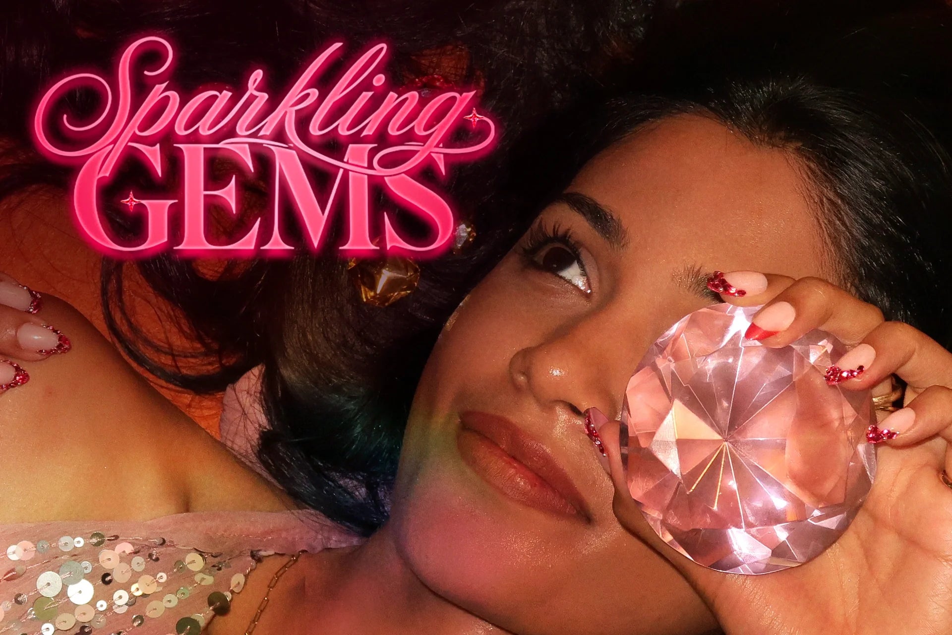 Model holding a pink gemstone with pink French tip nails adorned with sparkling red gems.