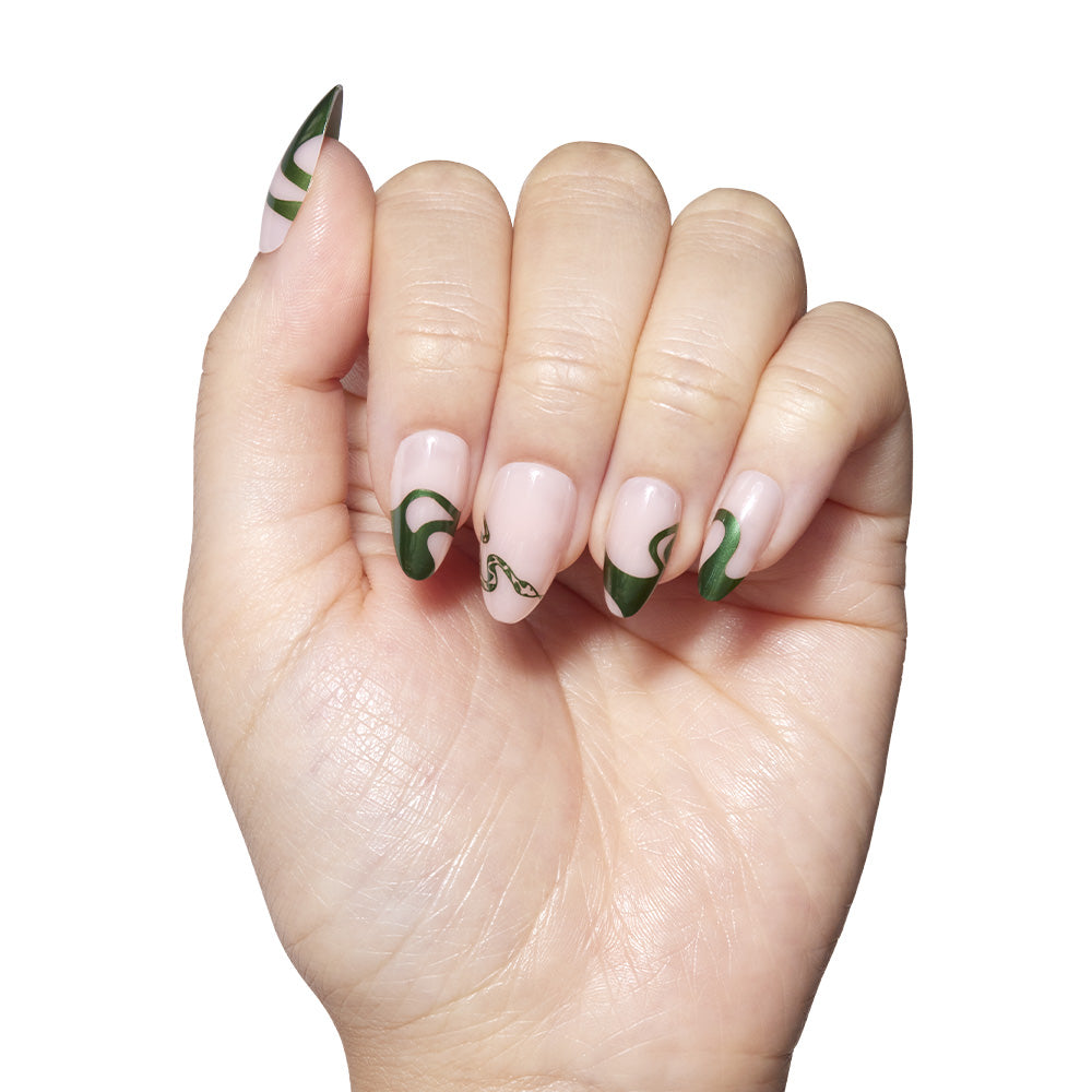 A hand with light skin and short almond manicured nails shows off green chrome emerald swirls on a nude base—highlighting glamnetic’s Parseltongue™ nail set—held against a white background. - Product image