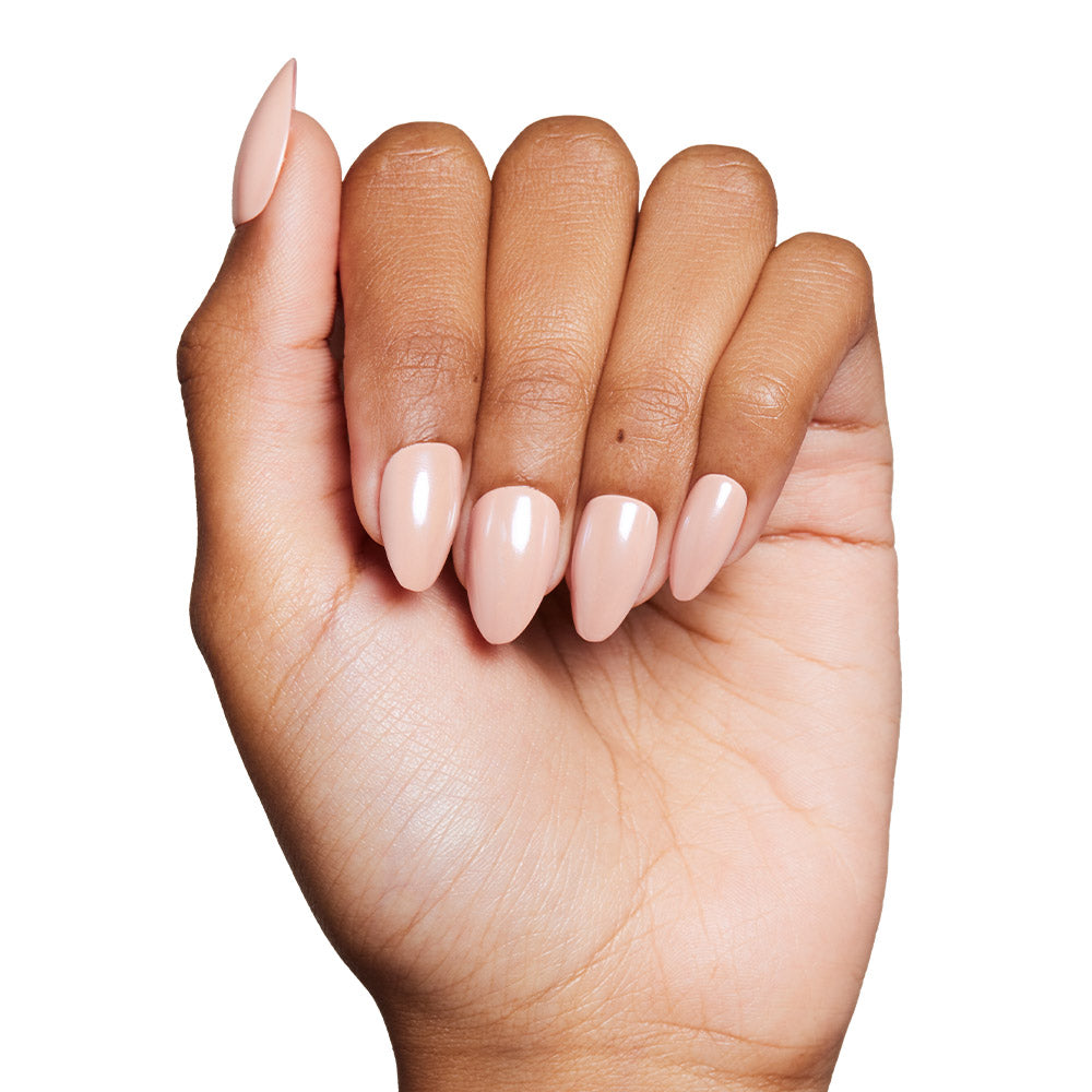 A hand with medium brown skin tone showcases the glamnetic Los Angeles nail set in a glossy nude-blush color. The short almond-shaped nails are neatly manicured and set against a clean white background. - Product image