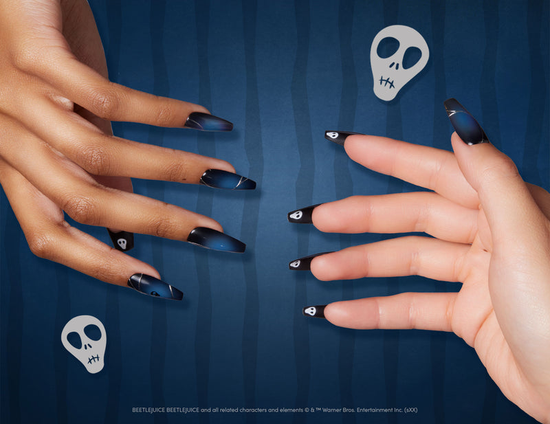 Two hands wearing Glamnetic x Beetlejuice press-on nails in a sleek dark blue and black gradient design, displayed over a striped blue background with white skull graphics