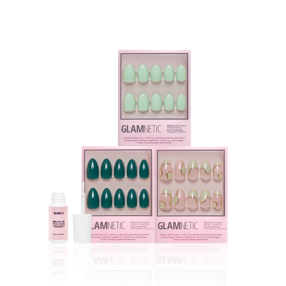 Three boxes of glamnetic Green Enchantment press-on nails in pastel and emerald green are shown with a small white nail glue bottle in front, highlighting their salon-quality durability on a white background. - Product image