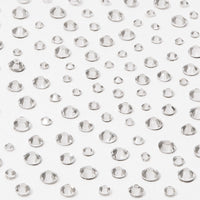 Multiple clear, round, faceted gems of different sizes are scattered on a white surface, creating a sparkling effect—perfect to use with glamnetic’s A Gem Nail Decal Stickers for stunning nail art designs.