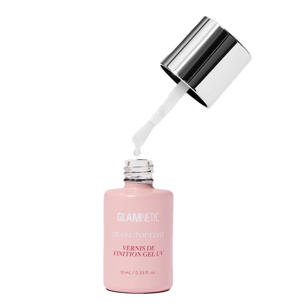 A pink bottle of glamnetic UV Gel Clear Top Coat with a silver cap is shown open, the brush applicator dripping clear gel for a glossy, salon-quality finish after curing under an LED UV lamp.