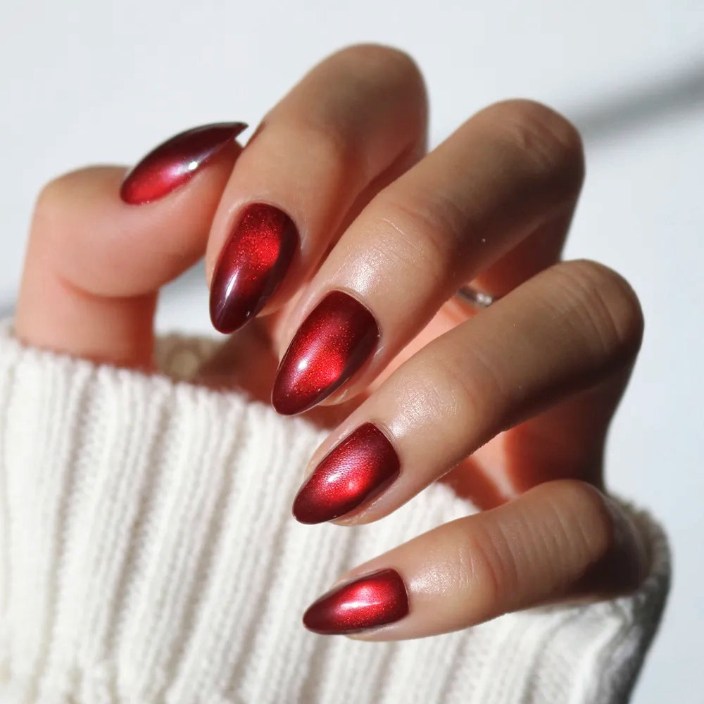 Hand with short almond press-on nails from the Glamnetic Frosted Cranberry set, featuring a deep red magnetic shimmer finish.