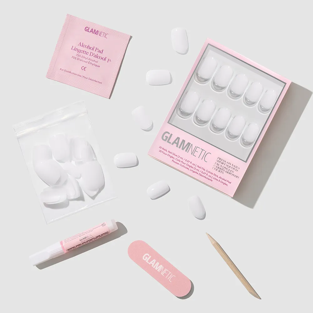 A flat lay of the glamnetic Clean Cut press-on nails kit, showing a box of white milky nails, extra nails in a pouch, pink nail file, cuticle stick, nail glue, and alcohol pad on a light grey background. - Product image