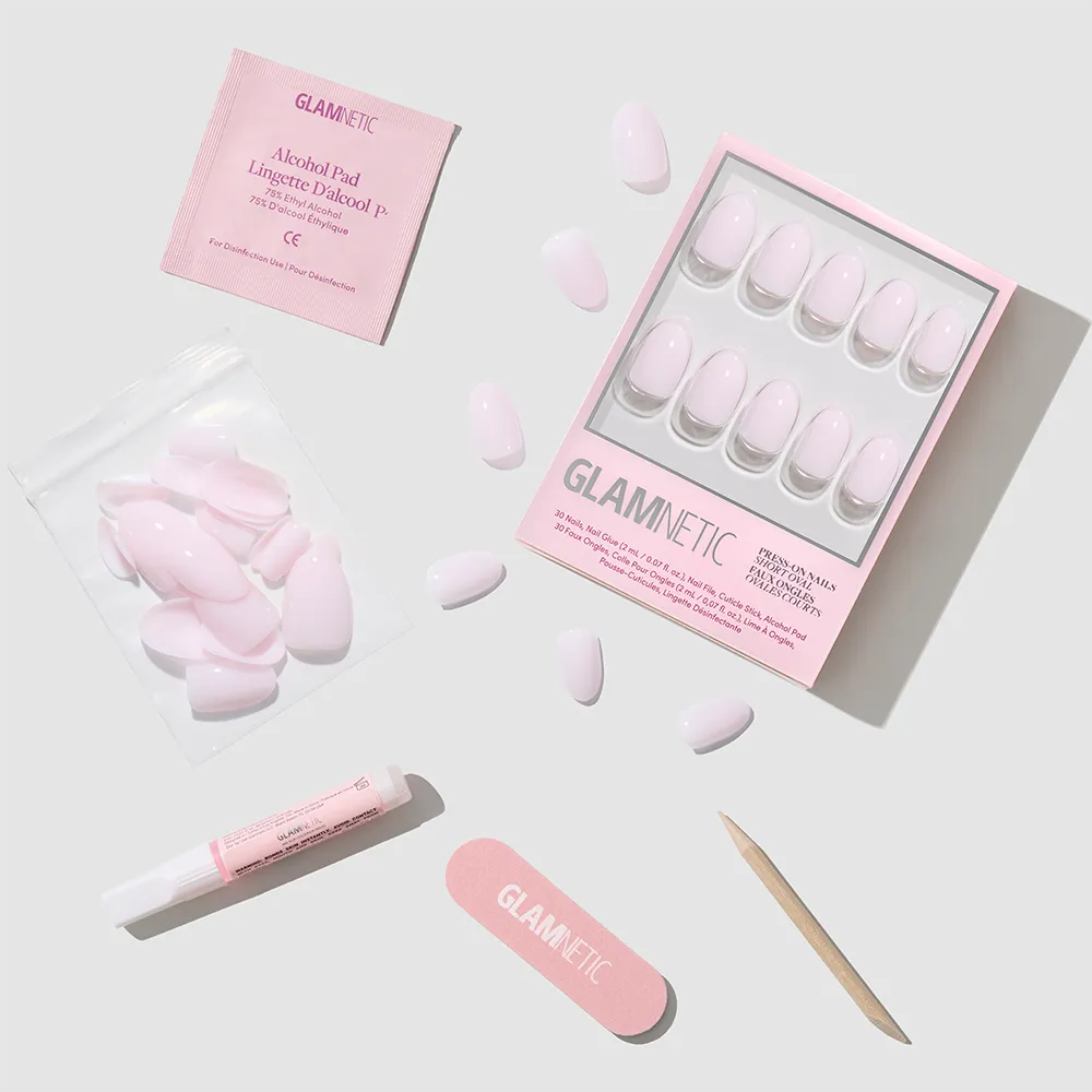 A flat lay of glamnetic's Doll Cheeks press-on nail kit, featuring short oval nails, extra loose nails, a nail file, cuticle stick, alcohol pad, and nail glue—everything for a salon-quality manicure on a light gray background. - Product image