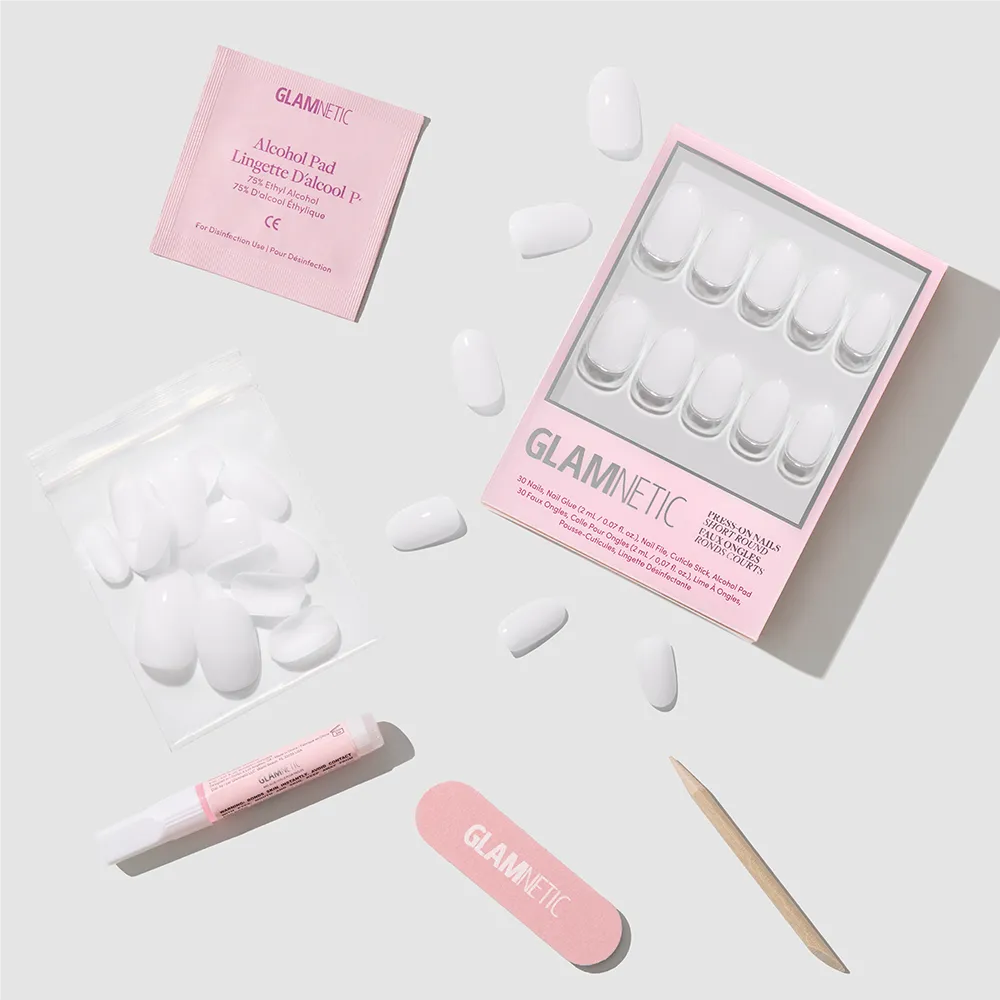 Glamnetic's Milk Bath Press-On Nails feature a chic short round shape and come with glue, alcohol pad, nail file, cuticle stick, and extra nails. All are arranged on a light gray background for the perfect milky mani. - Product image