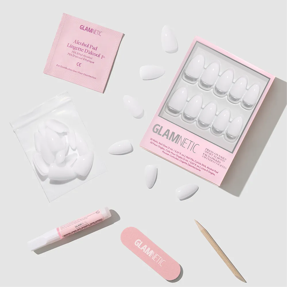 A flat lay of the glamnetic Milky White press-on nail kit includes short almond-shaped nails, a pink nail file, wooden cuticle stick, glue tube, alcohol pad, and extra nails for an easy salon-quality manicure at home. - Product image
