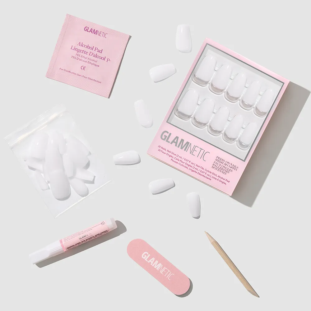A flat lay of the glamnetic Oat Milk press-on nails kit, showcasing stylish coffin-shaped milky nails, a pink nail file, alcohol pad, nail glue, cuticle stick, and extra nails arranged on a light gray background. - Product image