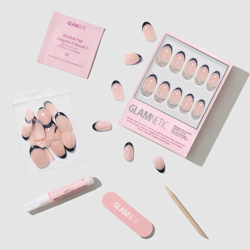 The Glamnetic Smoke Salt French tip press-on nails feature a glossy glazed finish in a short oval shape, and come with an alcohol pad, nail glue, nail file, wooden cuticle stick, and extra nails arranged on a light surface. - Product image
