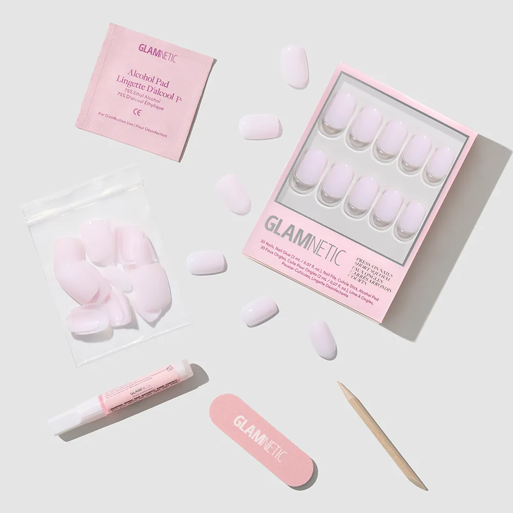 A set of glamnetic Soft Girl pink press-on nails in a short squoval shape, with nail file, cuticle stick, glue, extra nails, and alcohol pad arranged on a light gray background for a salon-quality mani at home. - Product image