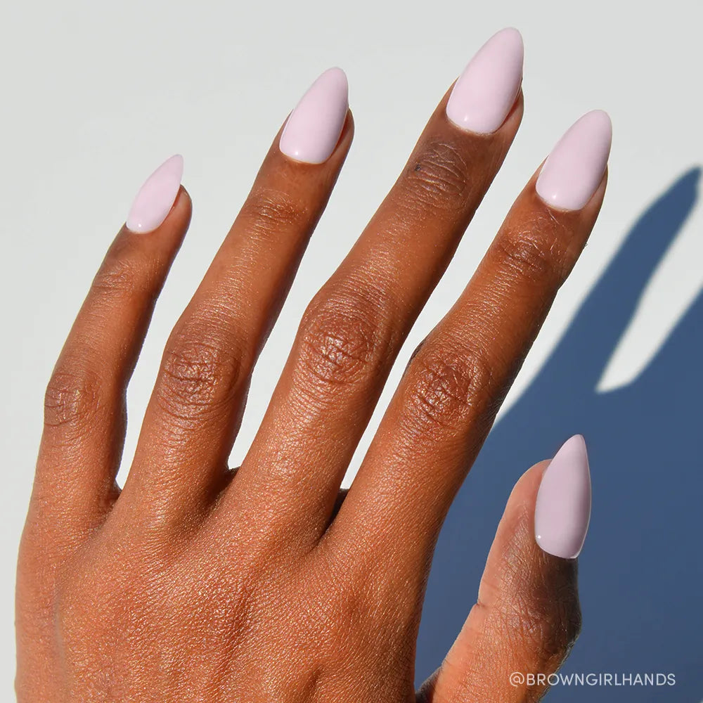 A hand with medium brown skin shows short almond nails painted glossy pink using glamnetic’s Sugar Doll press-ons, set against a pale background. - Product image