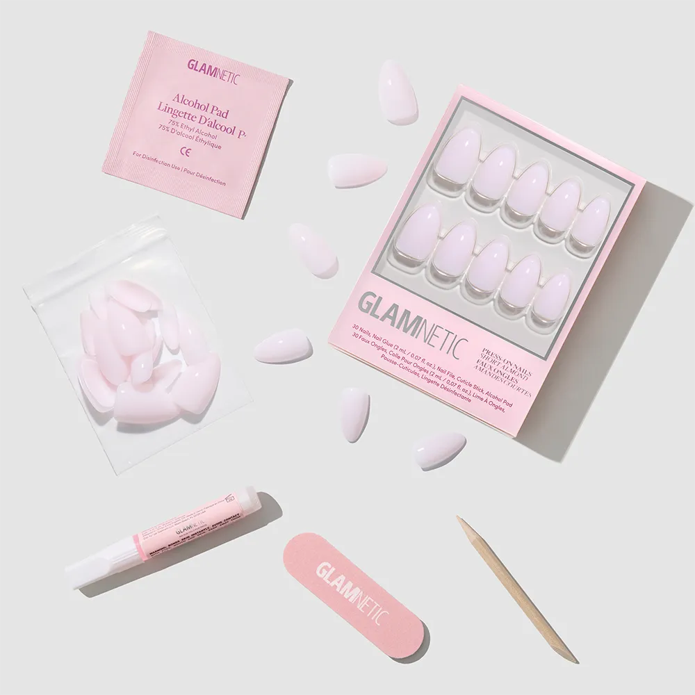 The glamnetic Sugar Doll set features glossy pink short almond press-on nails and includes nail glue, an alcohol pad, a wooden cuticle stick, a nail file, and extra nails—all arranged neatly on a light gray background. - Product image